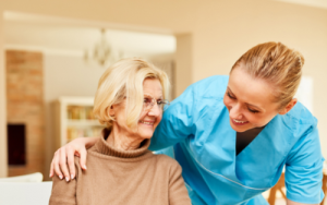 Nurse wearing blue scrubs, while leaning over white, older woman in a brown skivvy. Estate planning can include personal care, as well as writing a will.