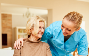 Nurse wearing blue scrubs, while leaning over white, older woman in a brown skivvy