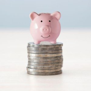 A piggy bank sits on a pile of coins, indicating capital gains and how they impact your financial situation.